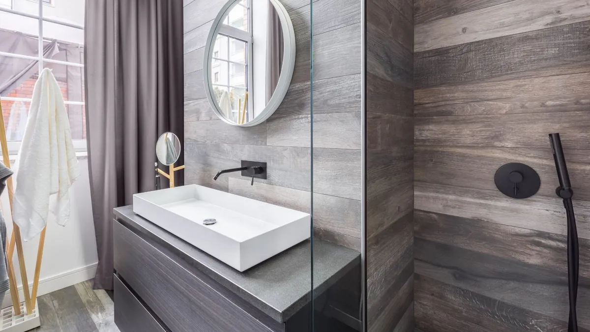 A modern bathroom with a stone-topped vanity, round mirror and walk-in shower