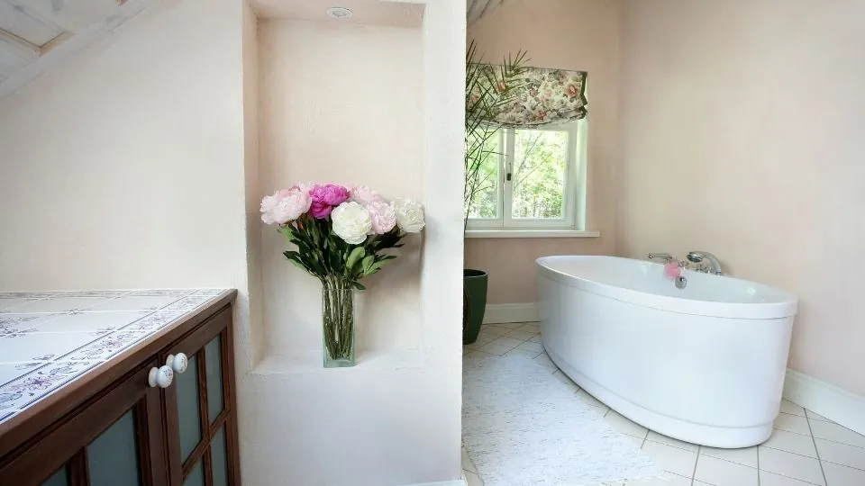 A freshly cleaned bathroom with a freestanding bath and fresh flowers on the vanity